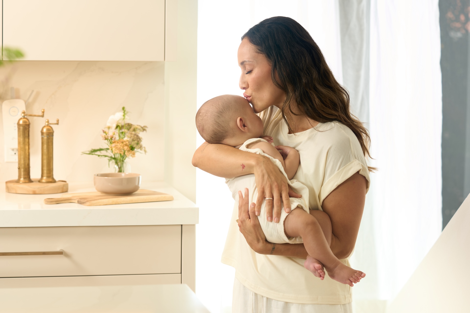 Mother kissing her newborn in a bright kitchen